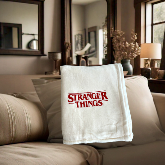 Stranger Things Christmas blanket with bold red logo on soft ivory throw, perfect for 80s nostalgia and holiday gifting