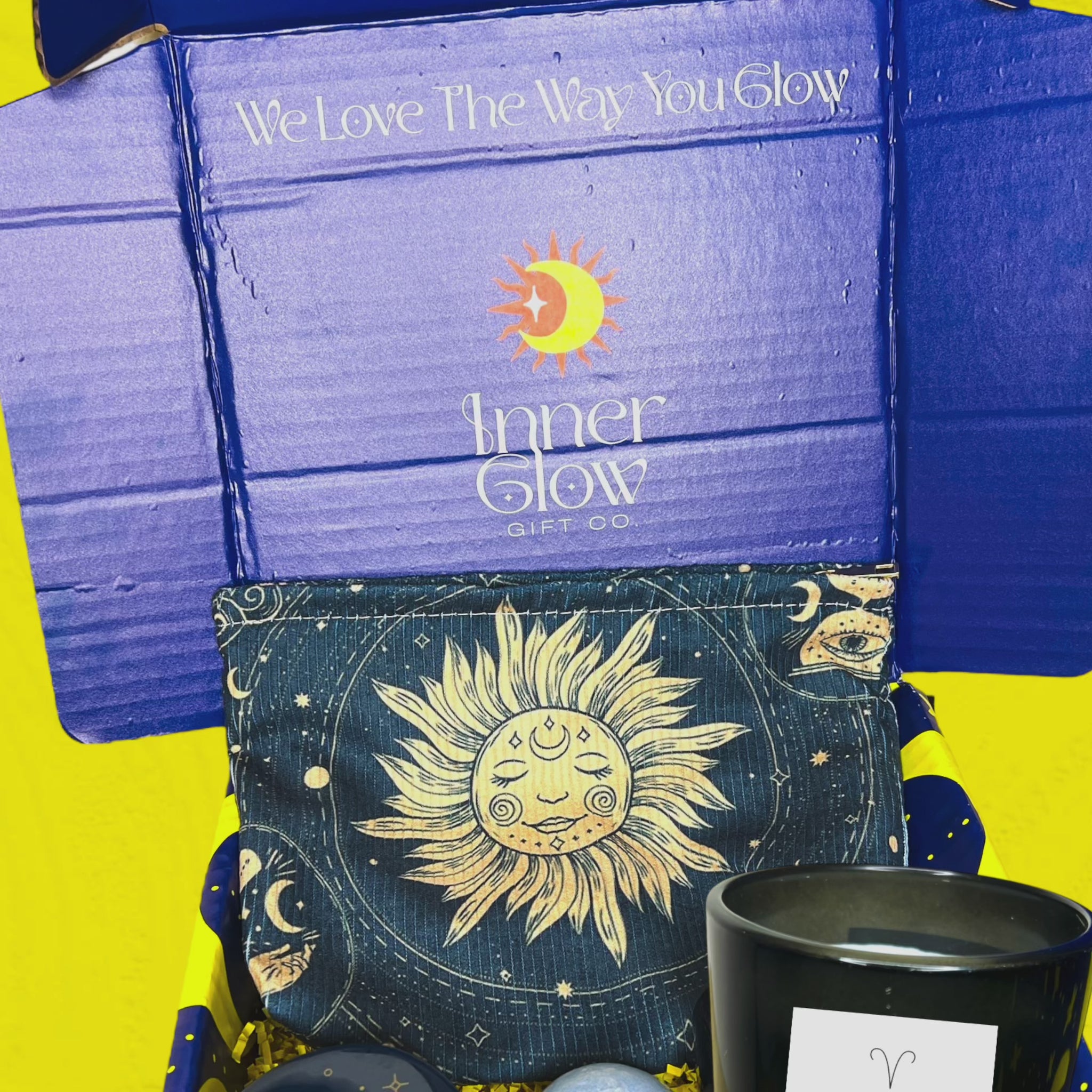 Celestial Glow Self-Care Gift Box featuring an Aries Zodiac Candle with blood orange and peach scent, a celestial-patterned pouch with a vibrant sun and moon design, a soothing blue bath bomb for relaxation, and  a midnight blue jar with gold constellation accents. All items are elegantly packaged in a vibrant blue keepsake box with celestial patterns and the tagline 'We Love The Way You Glow,' perfect for gifting or self-care enthusiasts